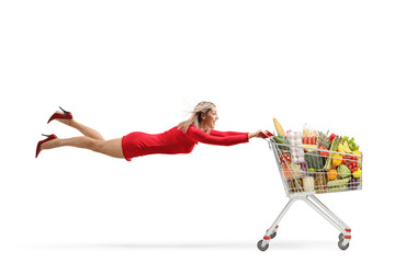 Attractive woman in a red dress flying and holding a full shopping cart