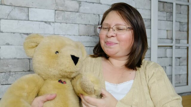 middle-aged adult woman with glasses communicates from home via video link, holds a teddy bear, gestures with her hands, remote education concept for children