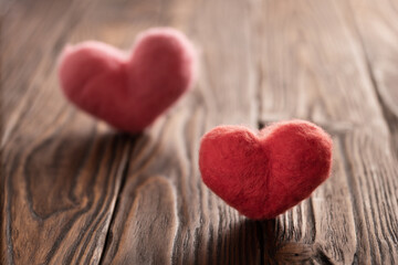 Two woolen backlit handmade hearts stand on the brown textured wooden boards. Valentine's day concept.