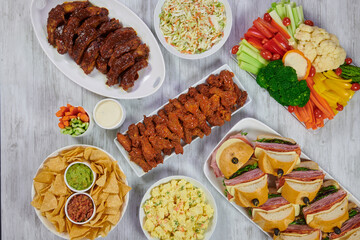 Party food spread with wings, ribs, potato salad, tortilla chips, guacamole, celery, carrots, hero sandwiches and Cole slaw.