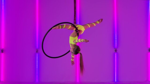 An acrobatic performance on an air hoop performed by a young circus performer. Teenager girl in a yellow leotard rotates under the dome. Slow motion.