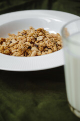 granola in a white plate on a table with a green tablecloth. Glass with milk
