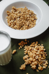 granola in a white plate on a table with a green tablecloth. Glass with milk