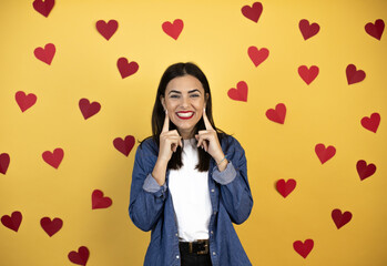Young caucasian woman over yellow background with red hearts smiling confident showing and pointing with fingers teeth and mouth