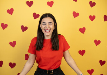 Young caucasian woman over yellow background with red hearts with a happy face standing and smiling with a confident smile showing teeth