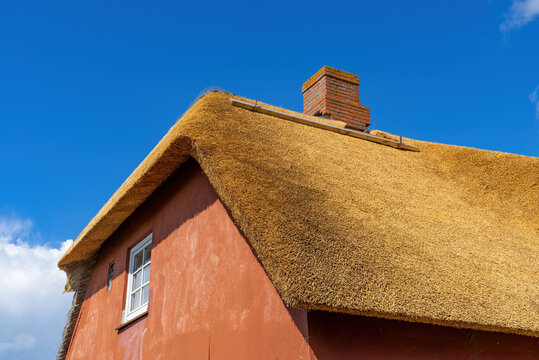 Reetdach auf rotem Haus mit Schornstein und blauem Himmel