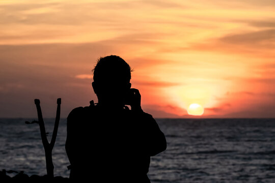 The silhouette of a male hobbyist photographer taking photos of a beautiful colorful sunset.