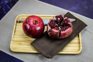 Two large large red pomegranate fruits. Whole red ripe pomegranate. Pomegranate fruit open which is divided into five parts which are held together on wooden tray on blue background. Knife next to it.