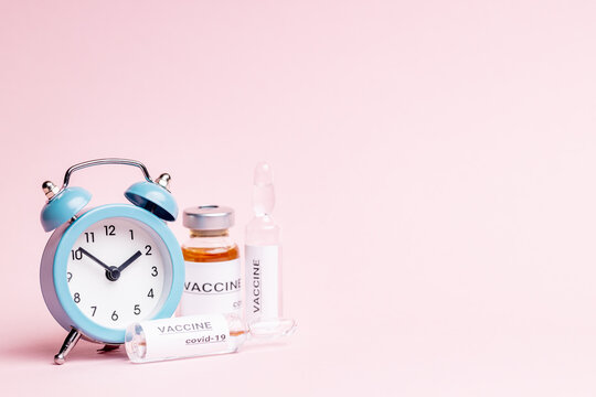 abstract vaccine vials and bottles for injection over pink background. alarm clock near vaccination drugs. vaccination concept