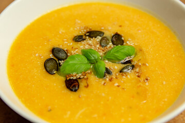 pumpkin cream soup with basil and pumpkin seeds served in a white ceramic bowl