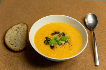 pumpkin cream soup with basil and pumpkin seeds served in a white ceramic bowl