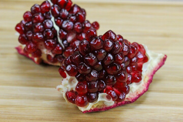 Two pieces of pomegranate with red seeds on a wooden tray. Pomegranate seeds. One piece in front and the other piece of ripe pomegranate fruit behind.