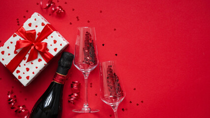 Concept for banner,greeting card for Valentine's day.Bottle of champagne wine,glasses with glittering candy in shape of heart,serpentine and gift box packed in white paper with red hearts,copy space