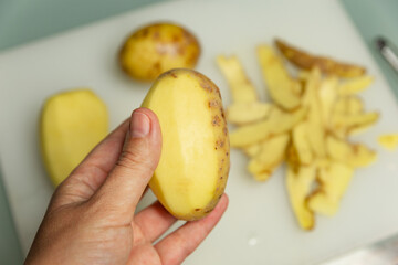 peeled potatoes in hand on a background of skin from potatoes