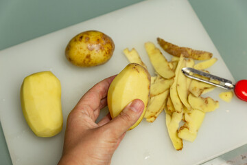peeled potatoes in hand on a background of skin from potatoes
