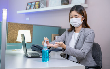 New normal style, Young businesswoman wearing face mask and using Sanitizer hand gel while working on a computer in the office.