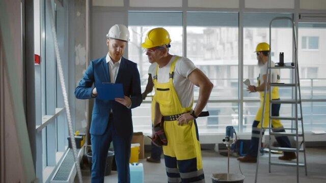 Contractor talking with builder in uniform and hardhat discussing office renovation plan