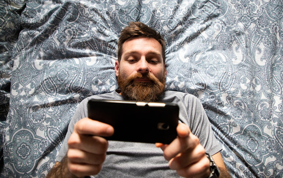 handsome man using smartphone in bed top view
