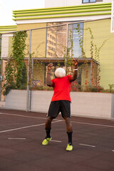 A black Portuguese football player in a red T-shirt catches the ball on his chest. The ball covers...