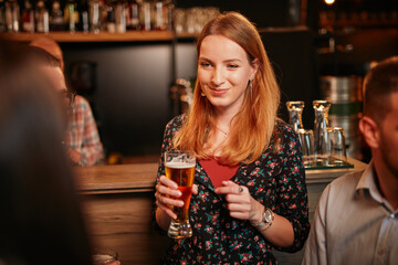 Small group of people leaning on bar counter, chatting and drinking beer.
