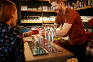 Small group of people leaning on bar counter, chatting and drinking beer.