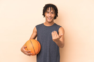 Young african american man isolated on beige background playing basketball and doing coming gesture
