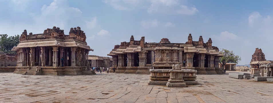 Hampi, Karnataka, India - November 5, 2013: Vijaya Vitthala Temple. Panorama shot of complex of beige-brown stone sanctuary buildings under light blue sky. People walking around add colors..