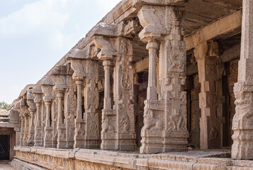 Obraz premium Hampi, Karnataka, India - November 5, 2013: Vijaya Vitthala Temple. Beige stone row of sculpted pillars along wall under light blue sky. Narasimha frescos galore.