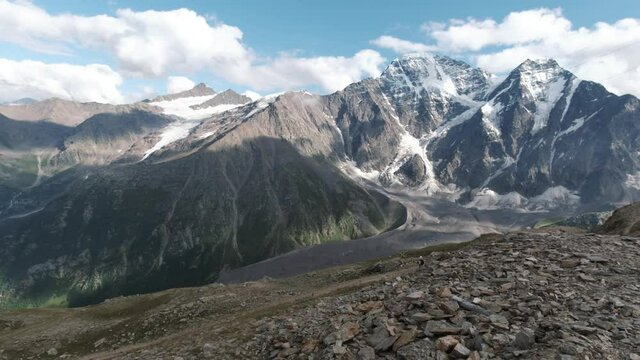 View from the hill top of endless snow capped mountain range. Clip. Breathtaking wild nature with clouds floating above huge mountains.