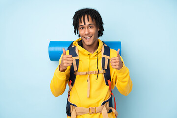 Young mountaineer african american man with a big backpack isolated on a blue background giving a...
