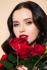 Fototapeta na wymiar brunette young woman with red lips holding roses isolated on pink