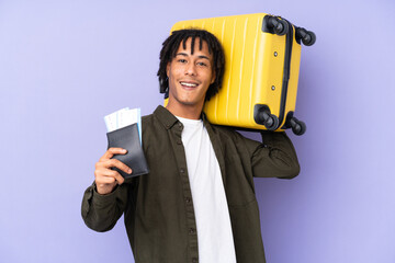 Young african american man isolated on purple background in vacation with suitcase and passport