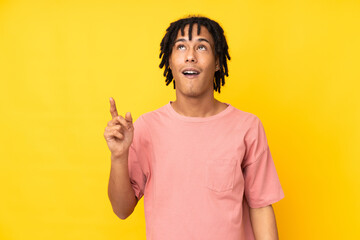 Young african american man isolated on yellow background pointing up and surprised