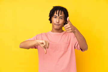 Young african american man isolated on yellow background making good-bad sign. Undecided between yes or not