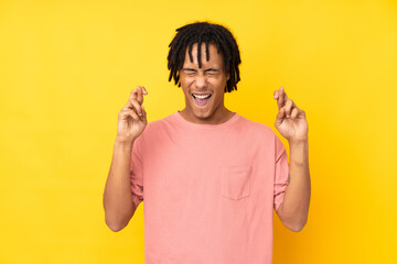 Young african american man isolated on yellow background with fingers crossing
