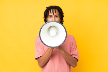 Young african american man isolated on yellow background shouting through a megaphone