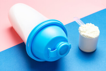 Shaker and scoop with protein on pink and blue background.