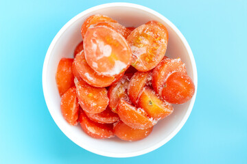 Frozen tomatoes in a white bowl on blue background top view.
