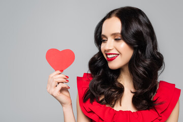 cheerful young woman holding red paper heart isolated on grey
