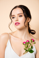 Fototapeta na wymiar sensual young woman looking away near flowers isolated on pink