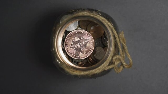 Close-Up of Bronze Bitcoin drop in Piggy Bank Jar of Coins with White Background