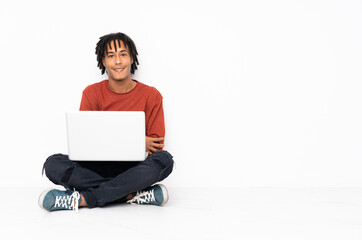 Young african american man sitting on the floor and working with his laptop posing with arms at hip and smiling