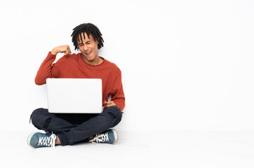 Young african american man sitting on the floor and working with his laptop doing strong gesture