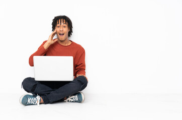 Young african american man sitting on the floor and working with his laptop with surprise and shocked facial expression