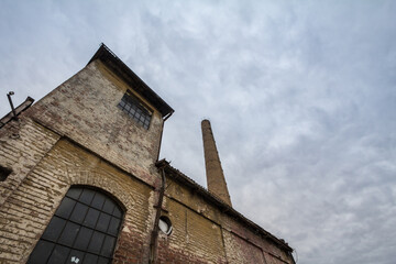 Fototapeta premium Abandoned factory and warehouse with its distinctive brick chimney in Eastern Europe, in Belgrade Serbia, former Yugoslavia, during a cloudy afternoon