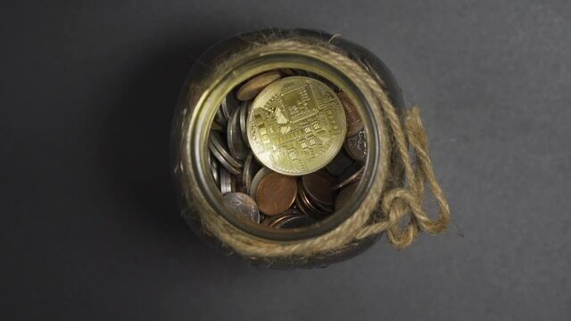 Close-Up of Gold Bitcoin drop in Jar of coins on black background