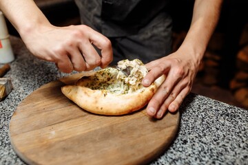 the hands of the cook prepare khachapuri on the kitchen table. cook a traditional Georgian treat of...