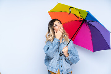 Teenager russian girl holding an umbrella isolated on blue background with surprise and shocked facial expression