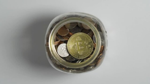 Close-Up of Gold Bitcoin drop in Piggy Bank Jar of Coins with White Background