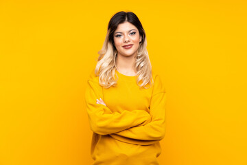 Teenager girl isolated on yellow background keeping the arms crossed in frontal position